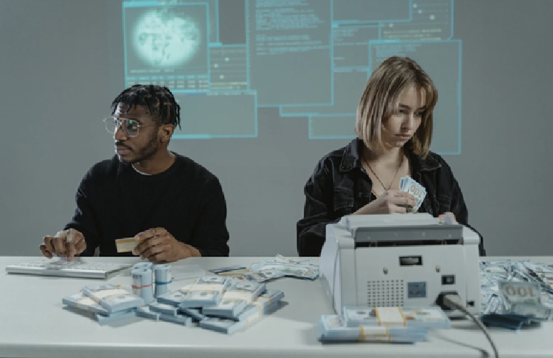 Two scammers in front of computers with money scattered around them